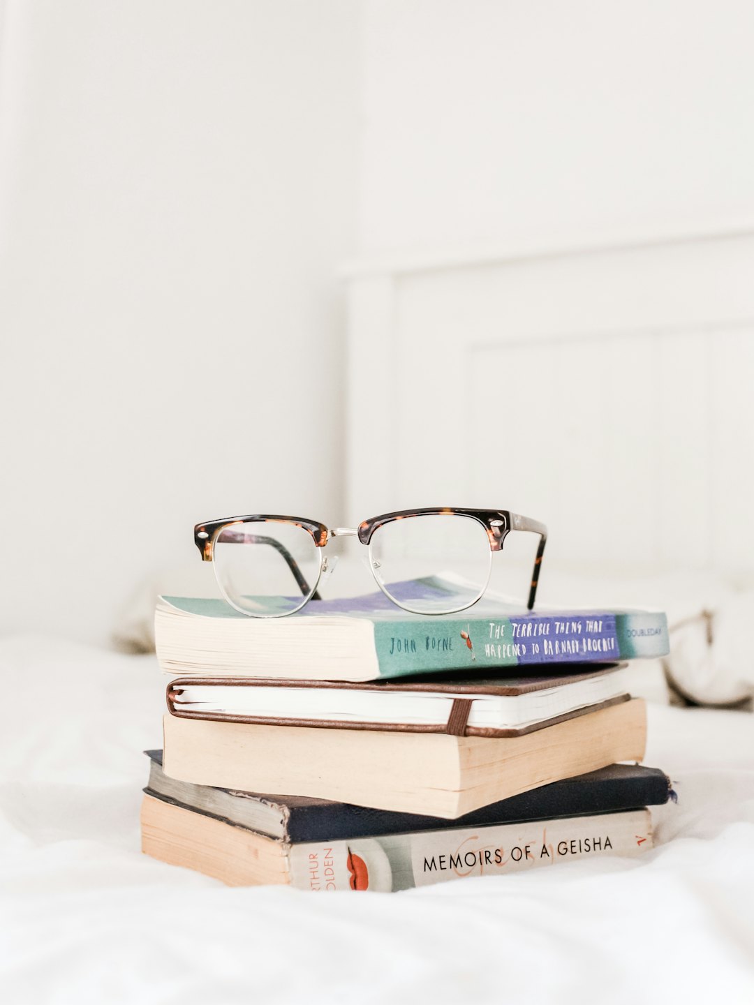 Books with reading glasses on a bed.