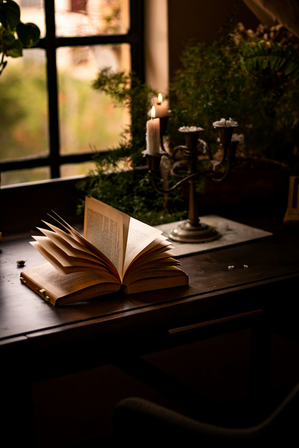 An open book rests on a wooden desk with two lit candles.